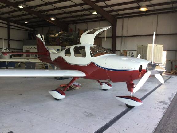 Red and white single-engine aircraft parked inside a hangar