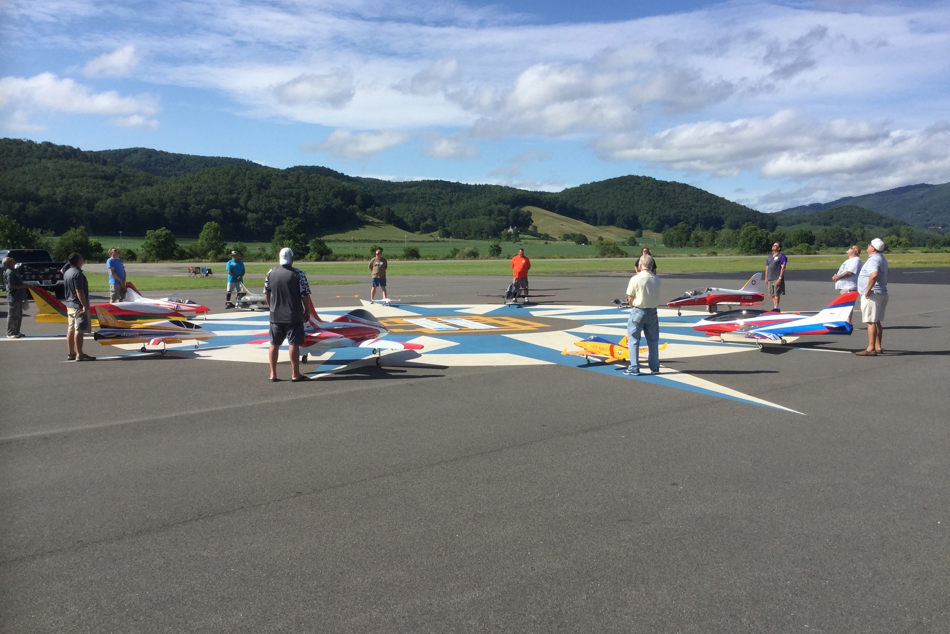 Pilots gathered with radio-controlled jets on the painted compass rose of the airport ramp